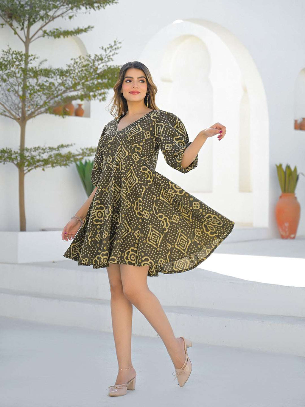 Woman in olive green Bandhani print short ethnic dress posing outdoors.