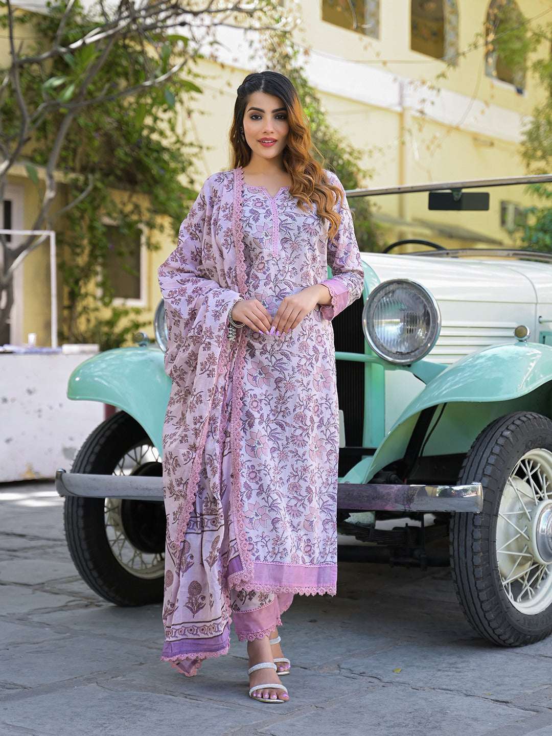 Woman wearing a light purple floral printed Indian ethnic suit standing by a vintage car.