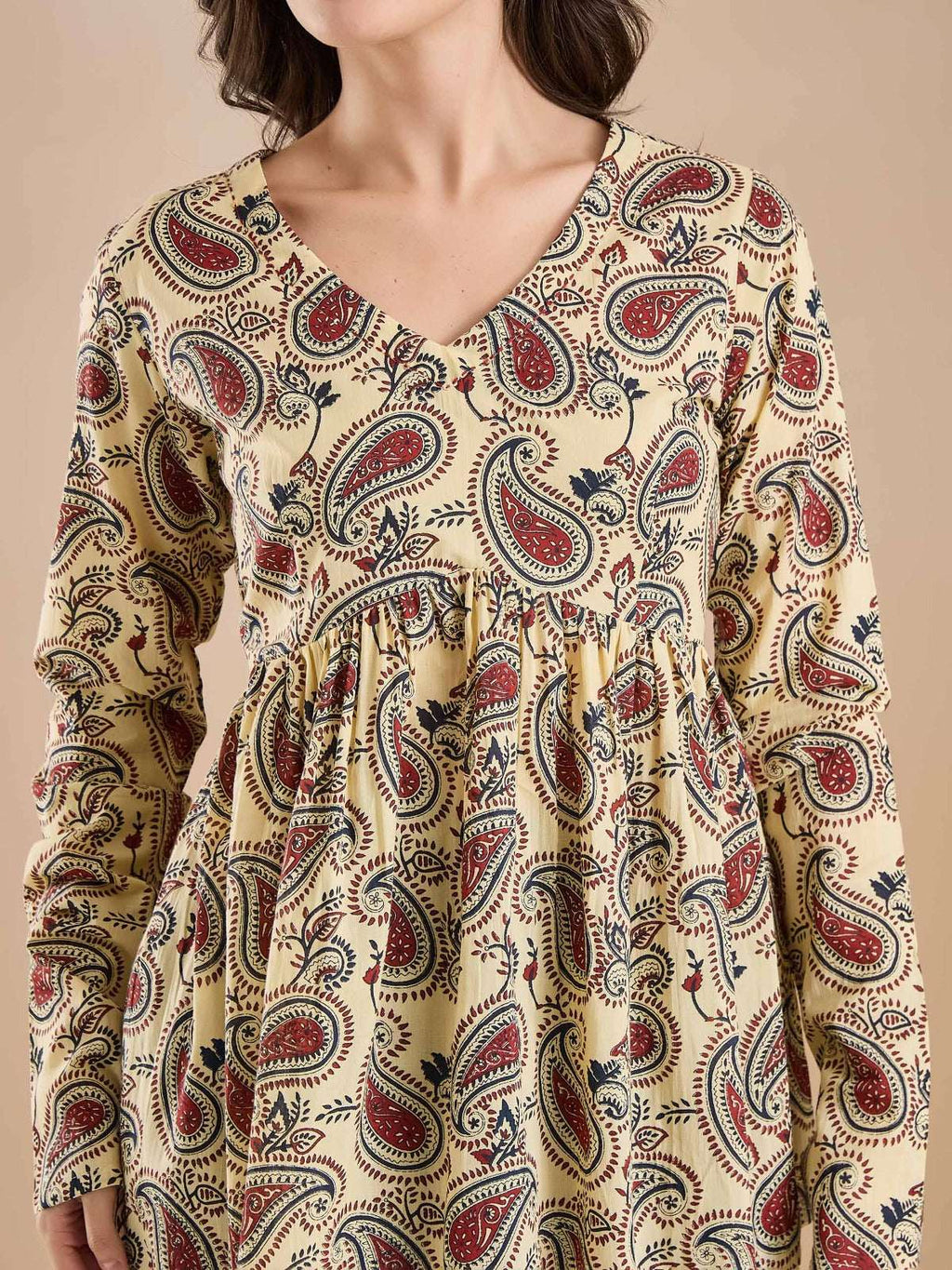 Woman wearing a cream long-sleeve ethnic dress with red and blue paisley print.