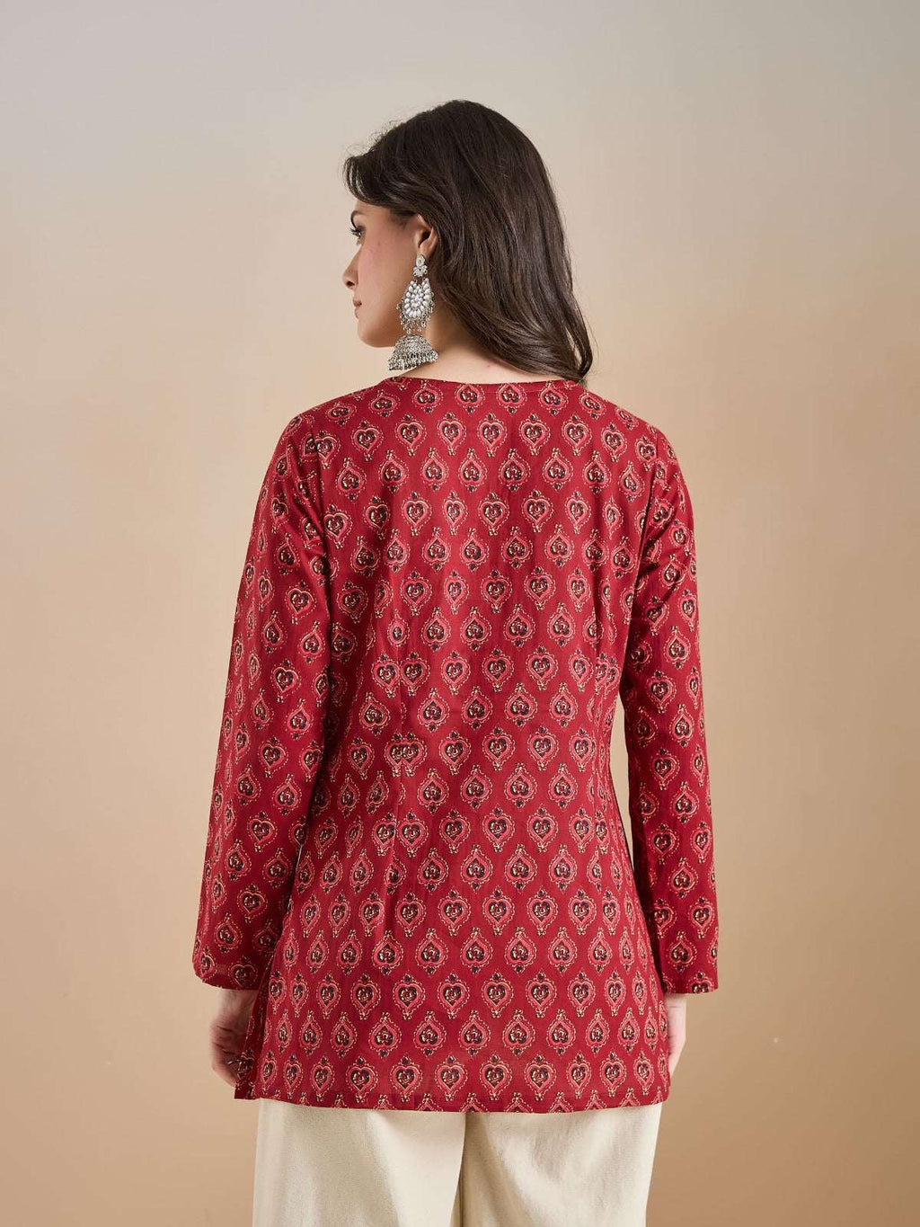 Woman wearing a red printed ethnic tunic with long sleeves and cream trousers.