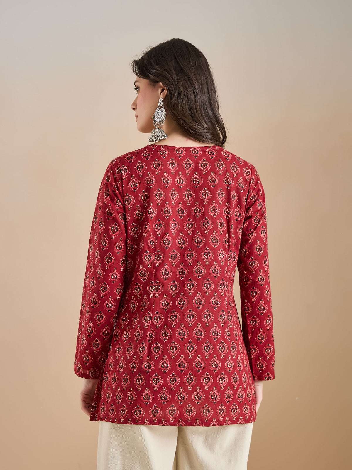 Woman wearing a red printed ethnic tunic with long sleeves and cream trousers.