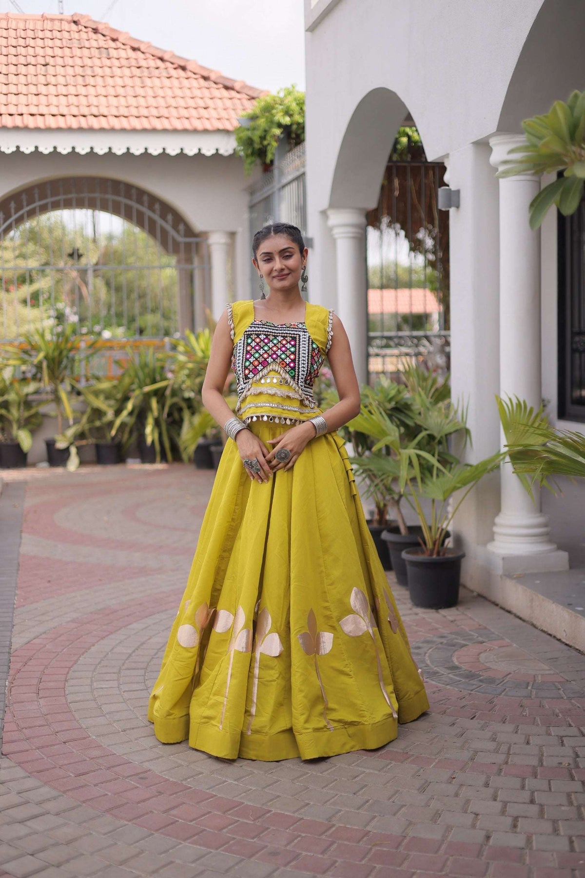 Woman wearing a yellow sleeveless lehenga choli with colorful mirror work embroidery.
