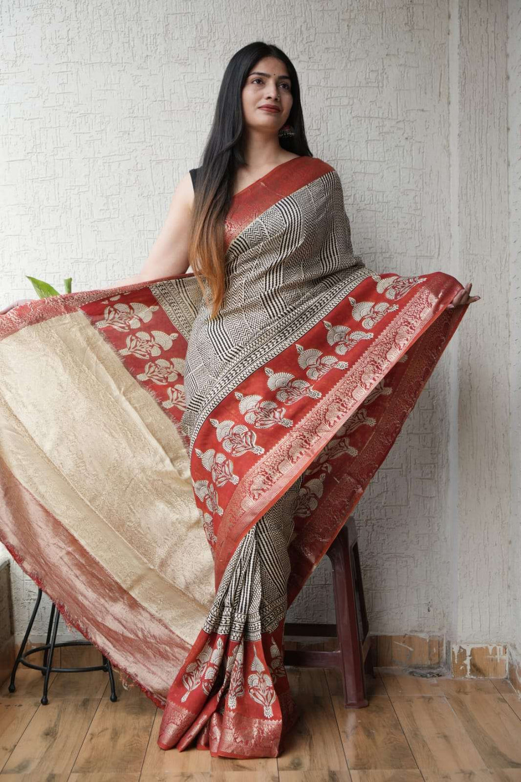 Woman wearing a traditional red and cream patterned silk saree with ethnic motifs.
