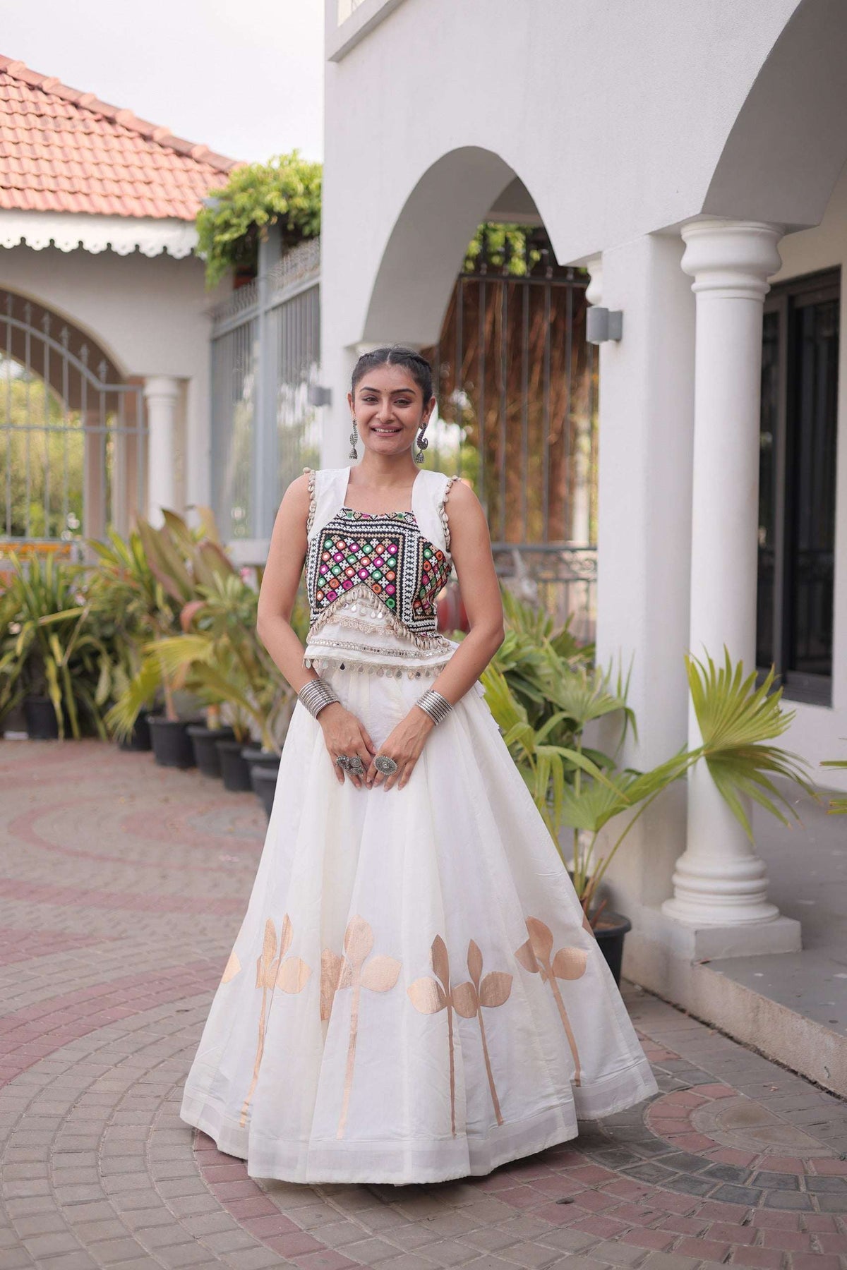 Woman wearing an elegant white lehenga choli with colorful embroidery and gold floral motifs.