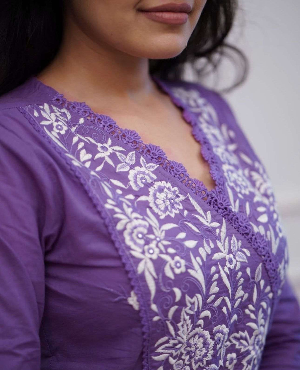 Woman wearing a purple ethnic tunic with intricate white floral embroidery and lace neckline.
