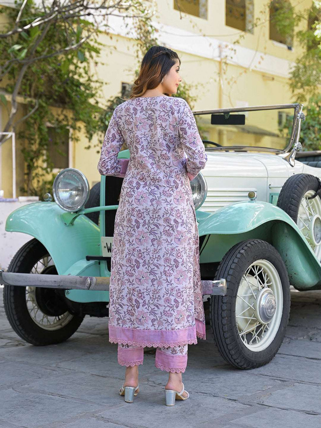 Woman in lavender floral print Indian ethnic kurta and palazzo set standing by a vintage car.
