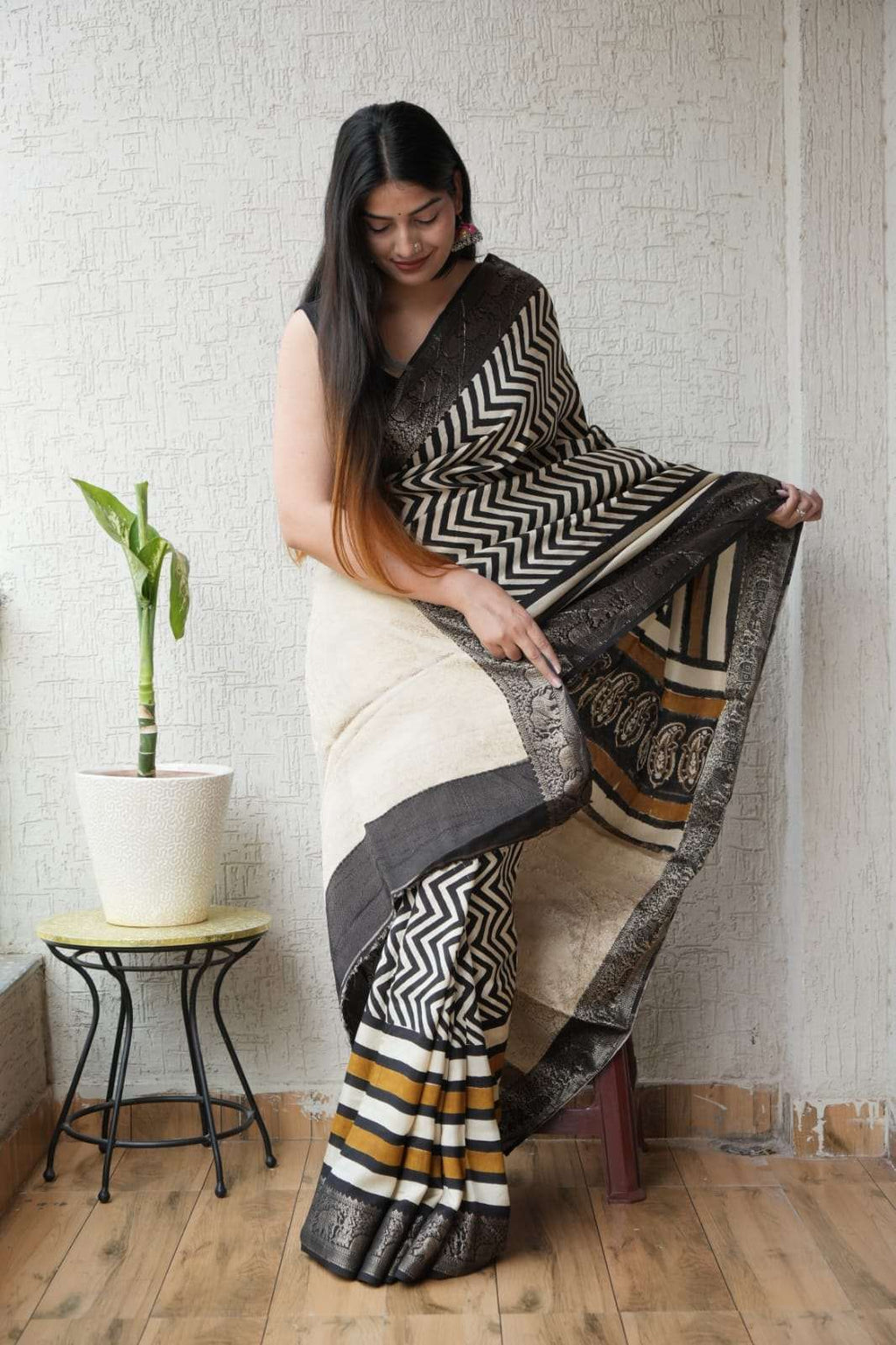 Woman wearing a black and cream ethnic saree with gold chevron patterns and border.