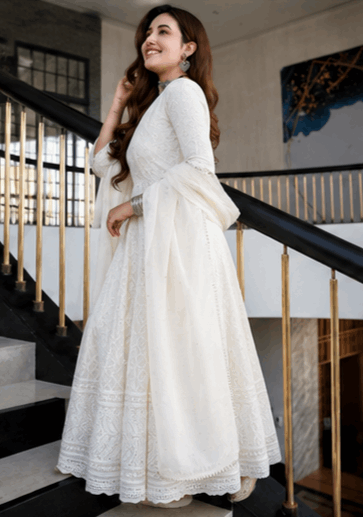 Woman wearing an elegant white embroidered Anarkali suit standing on a staircase.