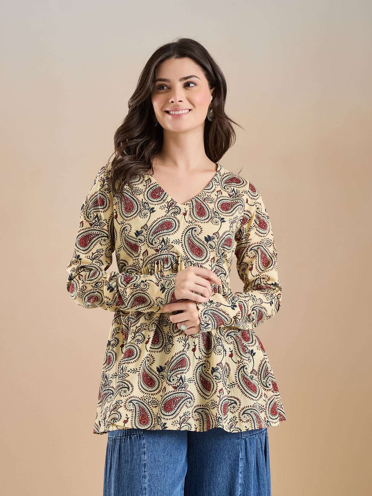 Woman wearing a cream paisley print v-neck long sleeve tunic top and blue denim trousers