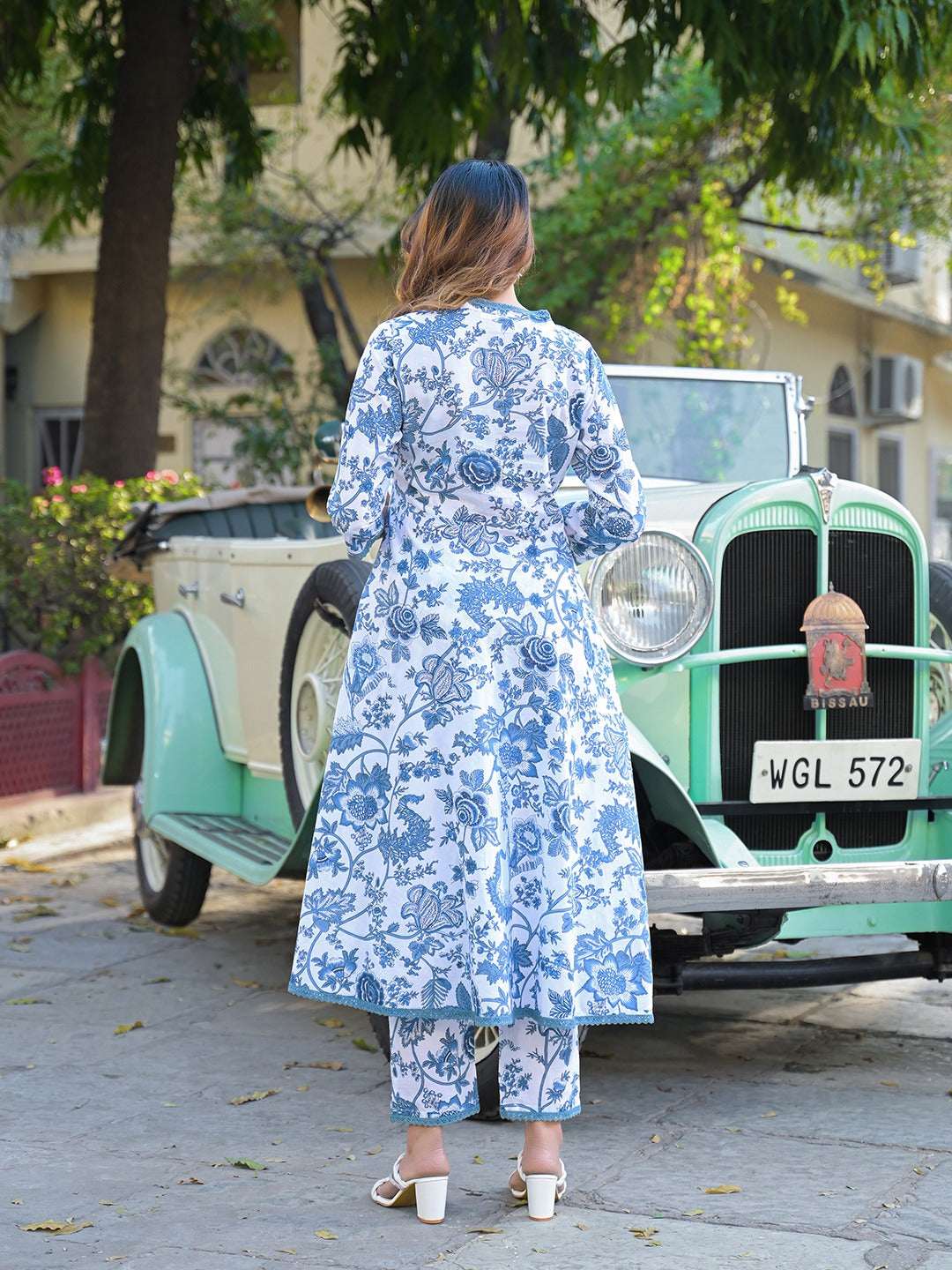 Woman in a blue and white floral printed ethnic dress standing by a vintage car.