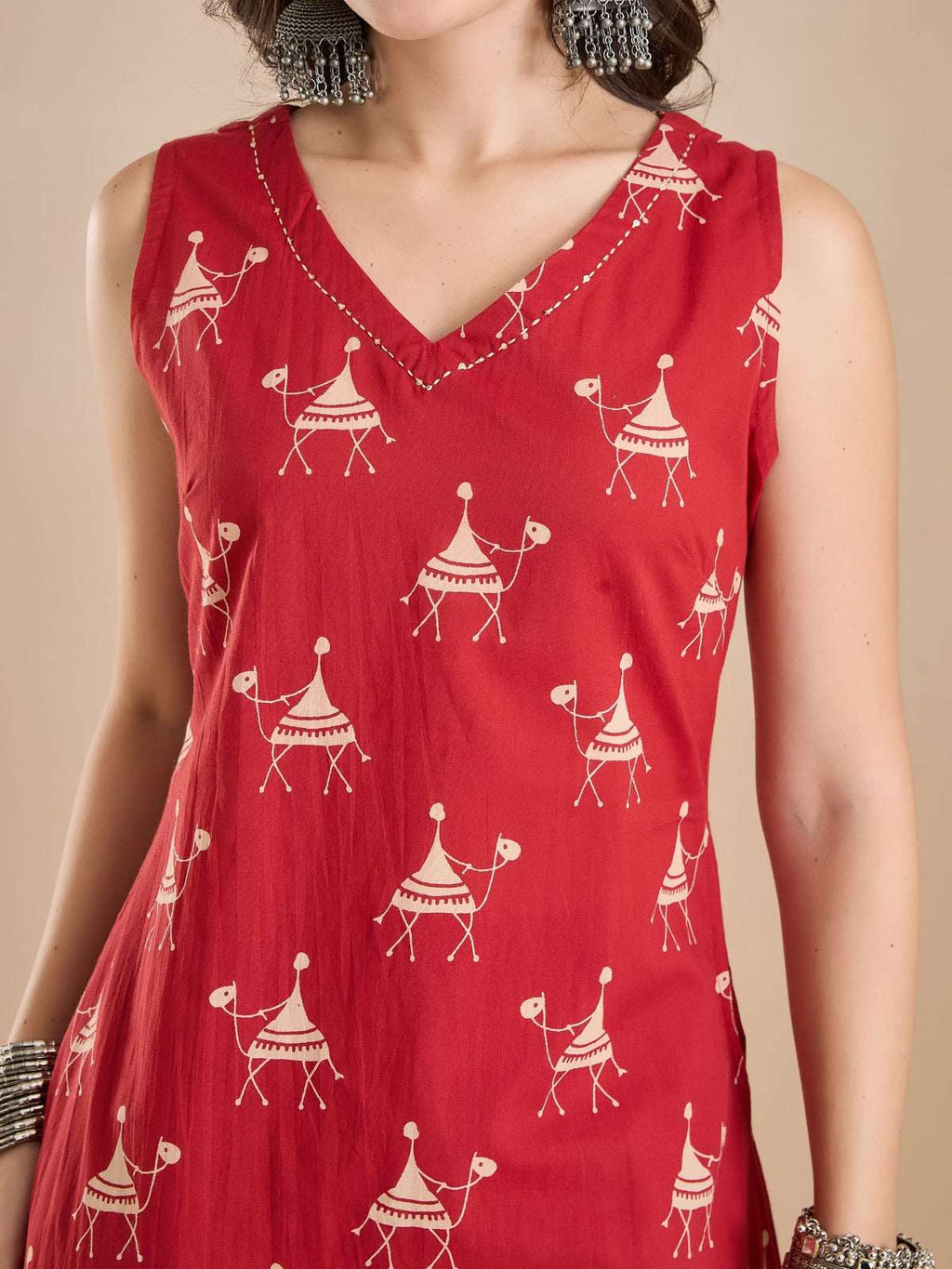 Woman wearing a red sleeveless V-neck ethnic tunic with white camel print patterns.