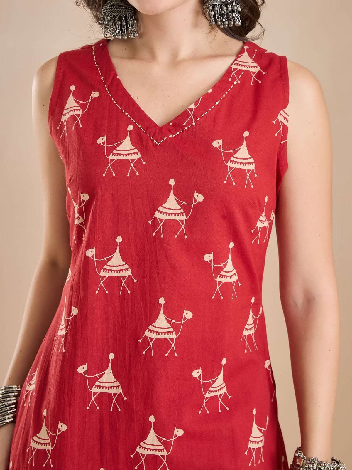 Woman wearing a red sleeveless V-neck ethnic tunic with white camel print patterns.