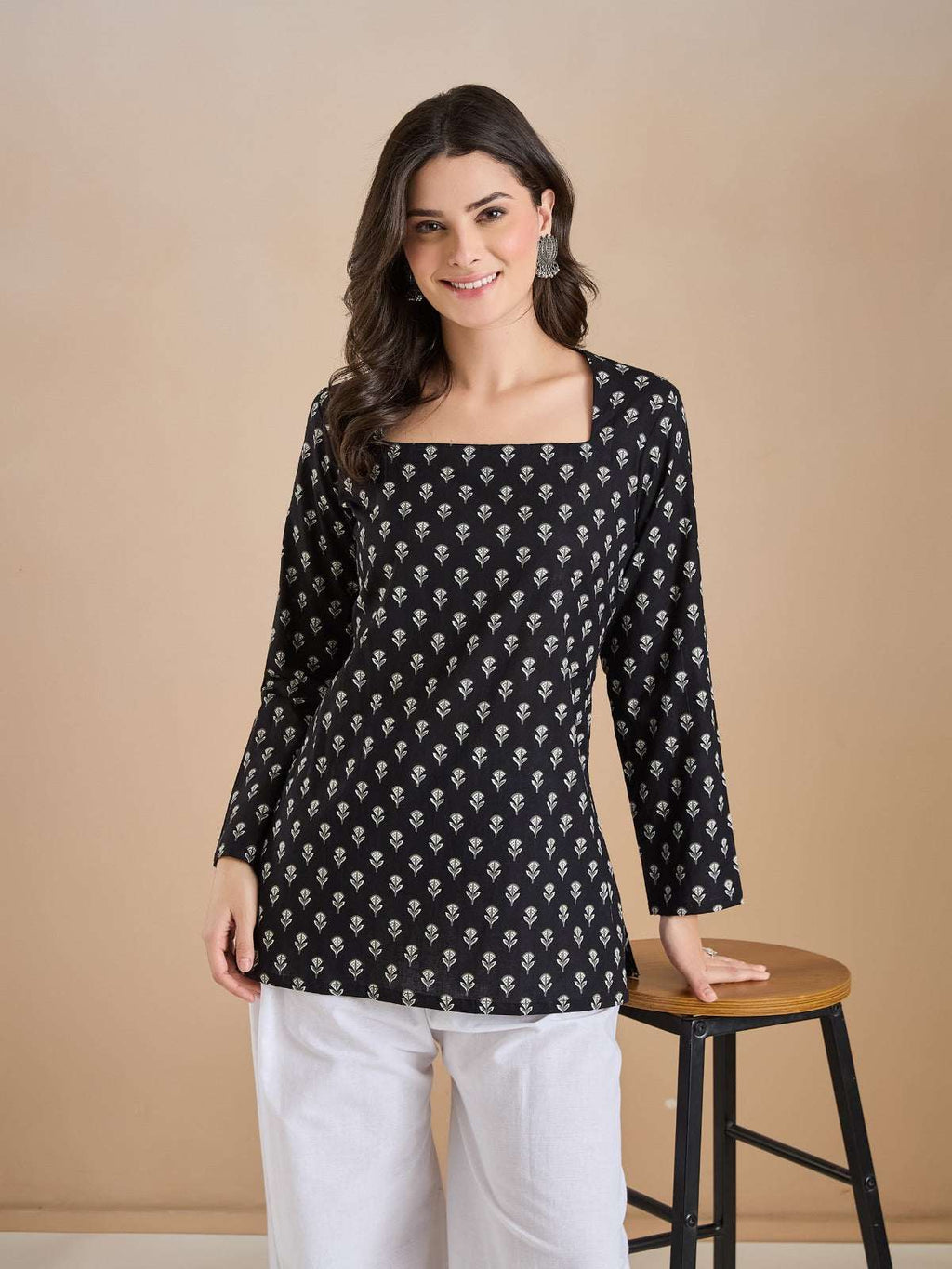 Woman wearing a black floral print tunic with white trousers