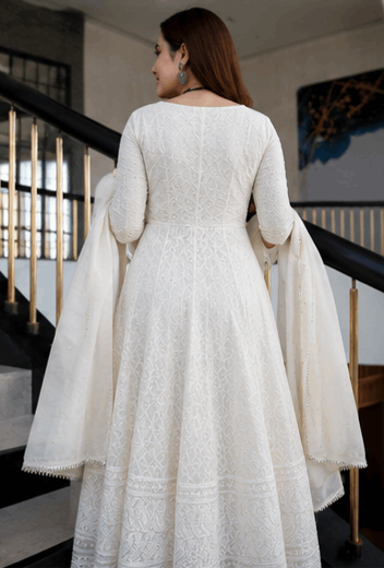 Woman in elegant white ethnic Anarkali dress with intricate embroidery standing on stairs