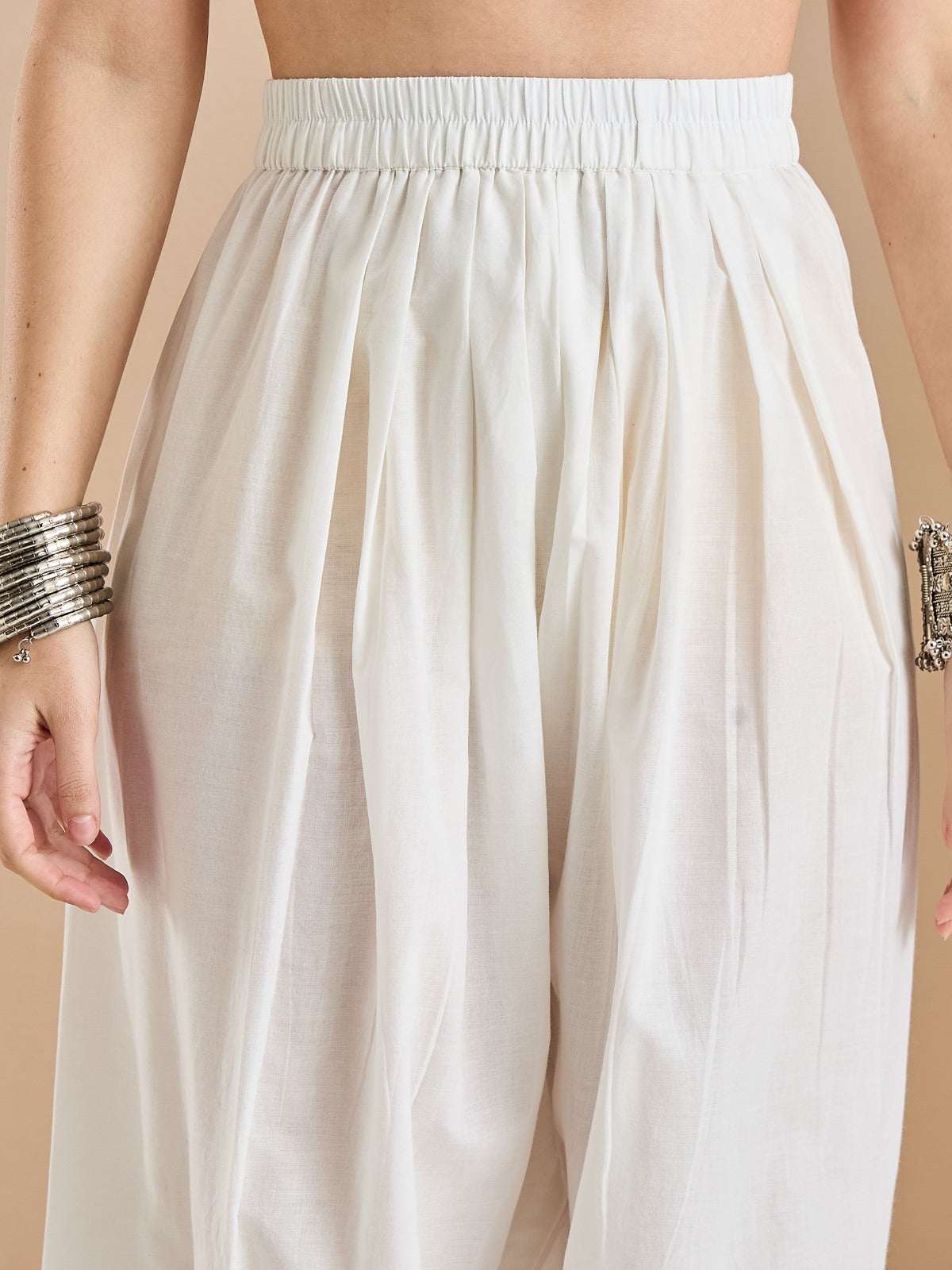 Woman wearing white pleated high-waisted ethnic palazzo pants with silver bangles.
