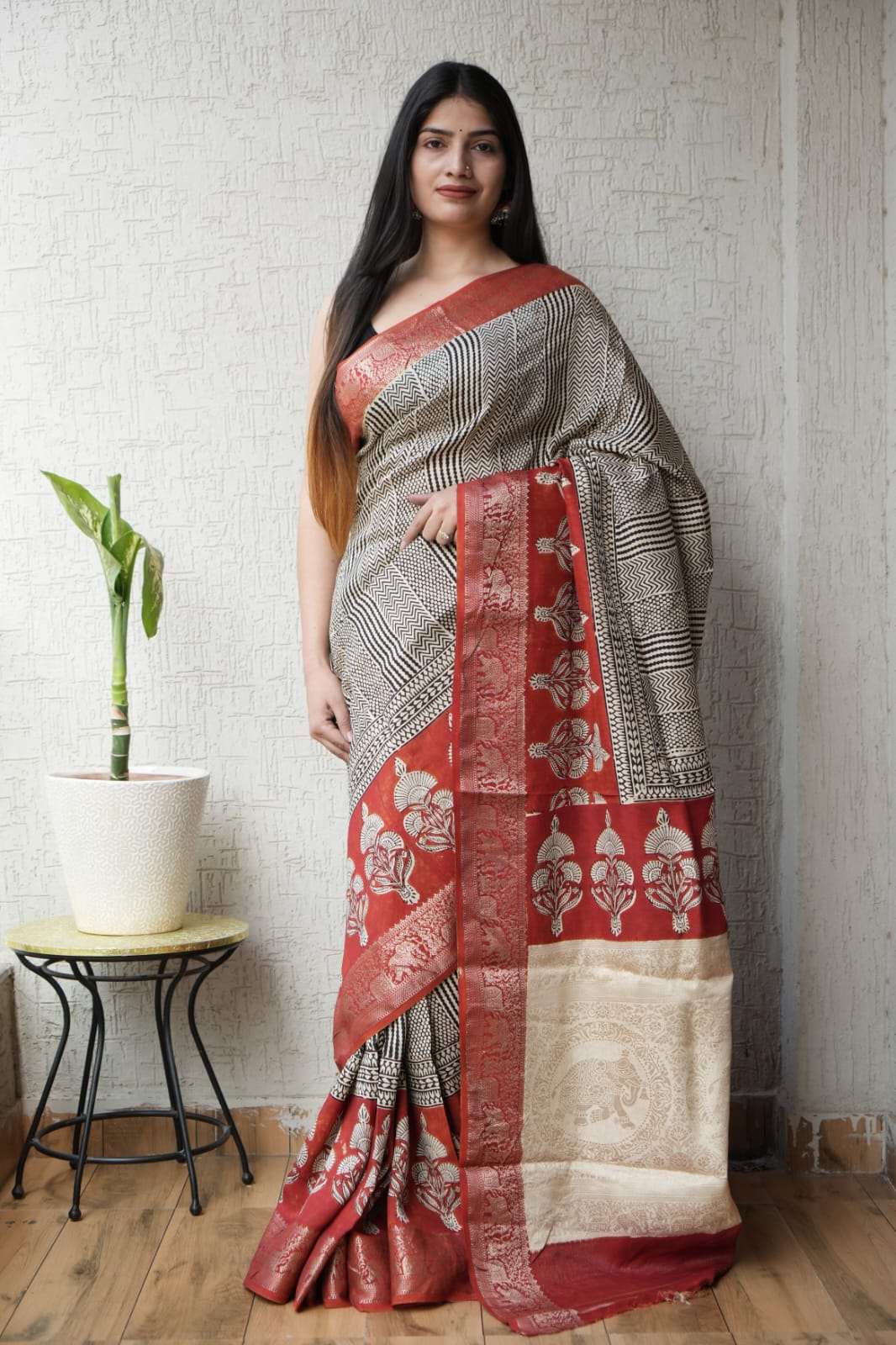 Woman wearing an elegant black and cream patterned saree with a red floral border.