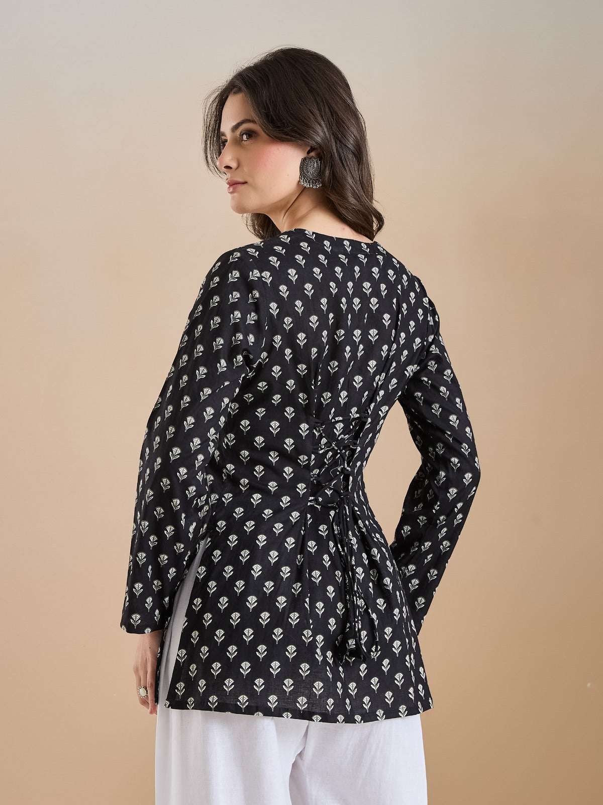 Woman wearing a black long-sleeve floral print tunic with tie-back detail and white trousers.