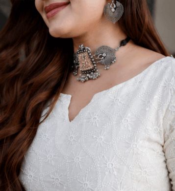 Woman wearing an ethnic silver oxidized choker necklace and matching earrings with a white embroidered tunic.