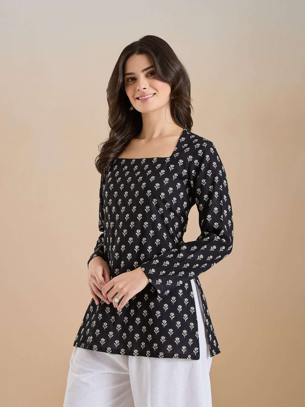 Woman wearing a black floral print long sleeve tunic with white trousers.