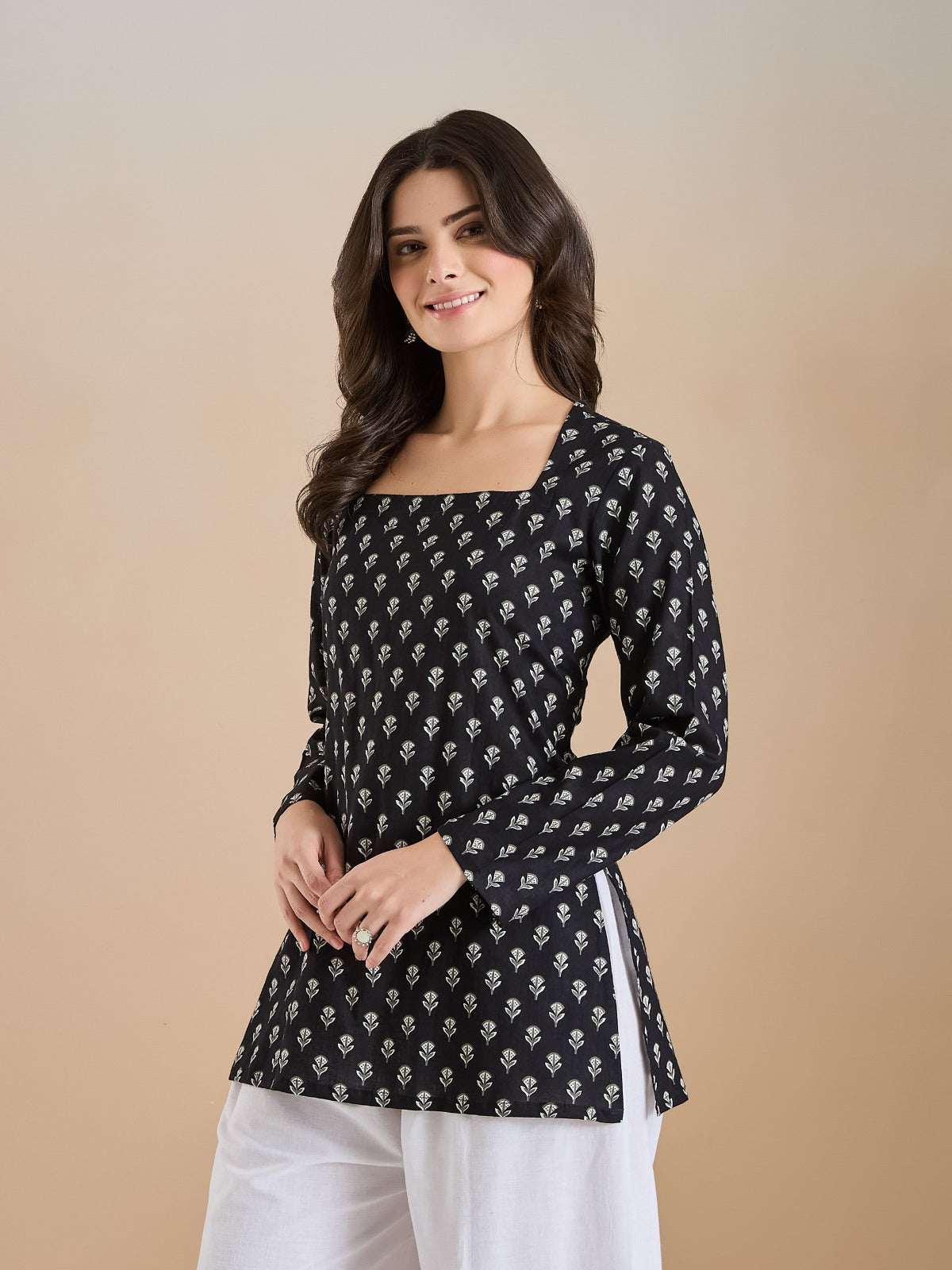 Woman wearing a black floral print long sleeve tunic with white trousers.