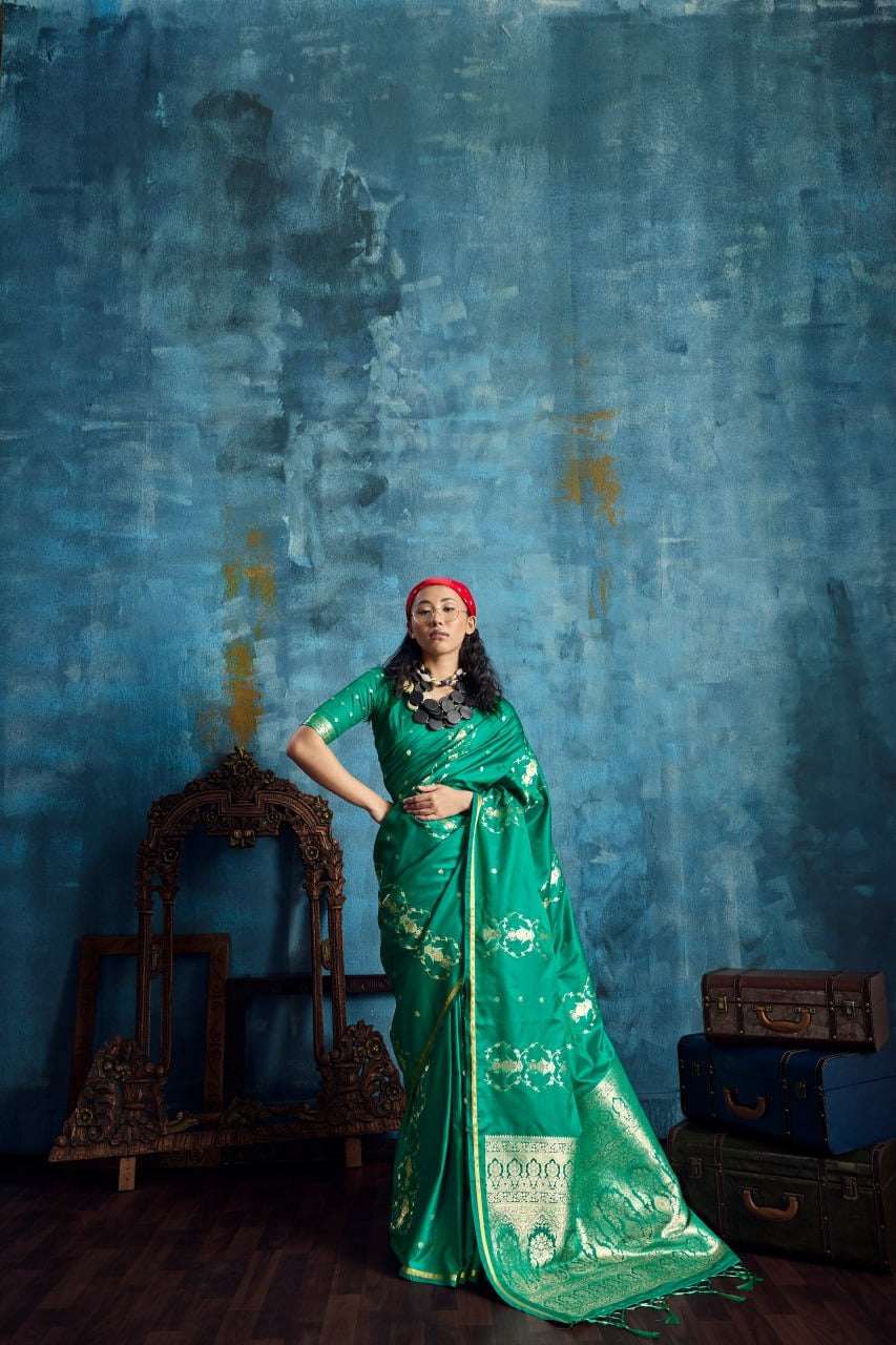 Woman in elegant green silk Banarasi saree with gold zari work against a blue backdrop.