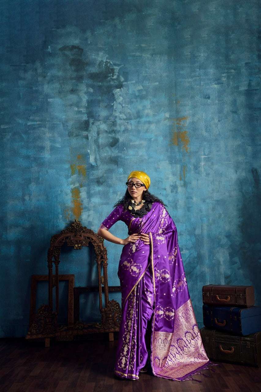 Woman in elegant purple silk saree with gold floral patterns and yellow headwrap.