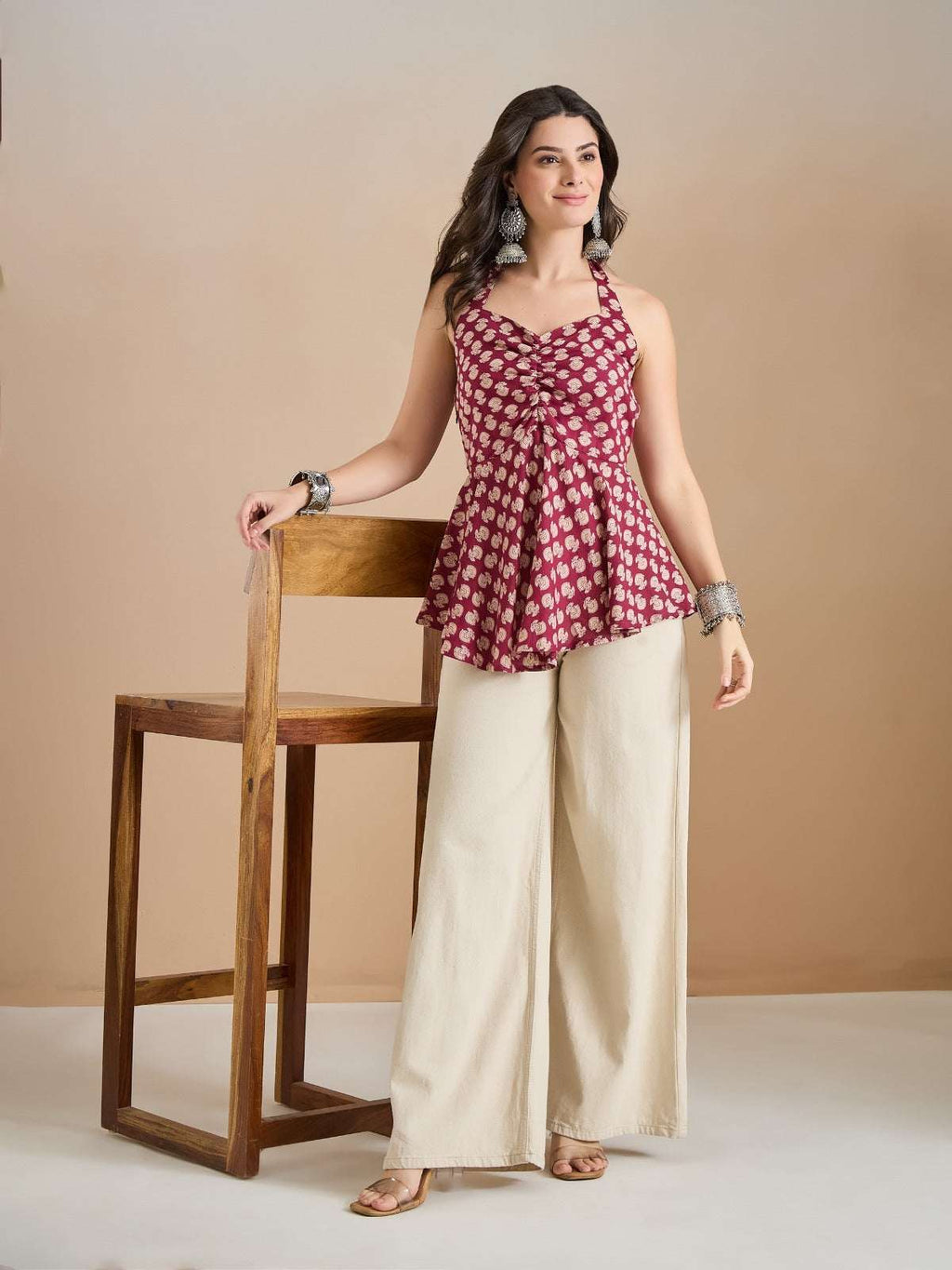 Woman wearing a maroon floral print halter top and cream wide-leg palazzo pants.