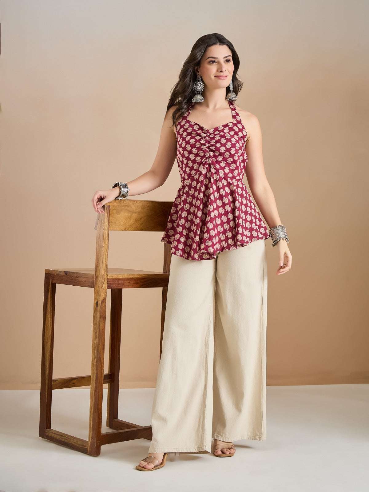 Woman wearing a maroon floral print halter top and cream wide-leg palazzo pants.