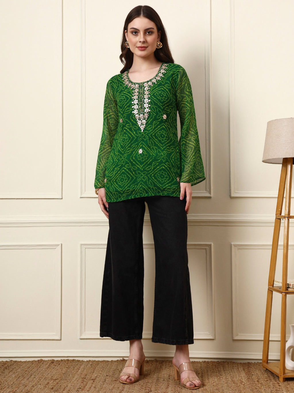 Woman wearing a green patterned long tunic with silver embroidery and black wide-leg pants.