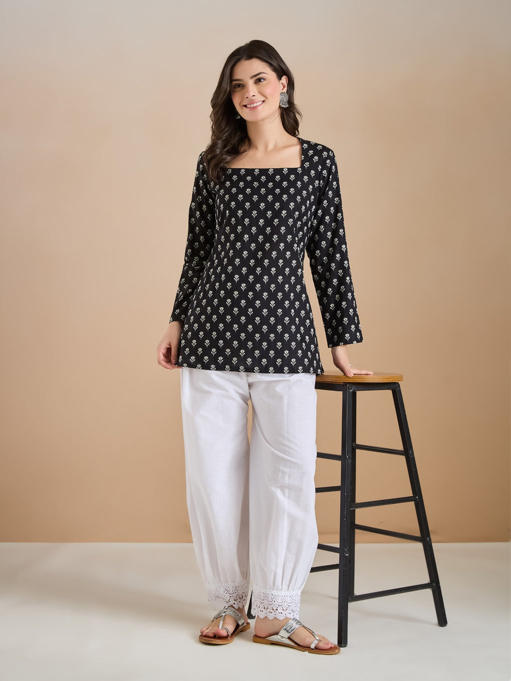 Woman wearing a black floral print long tunic with white lace-trim palazzo pants.