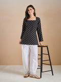 Woman wearing a black floral print long tunic with white lace-trim palazzo pants.