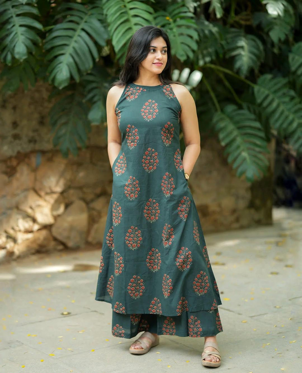 Woman wearing a dark green ethnic printed sleeveless A-line dress with matching pants.