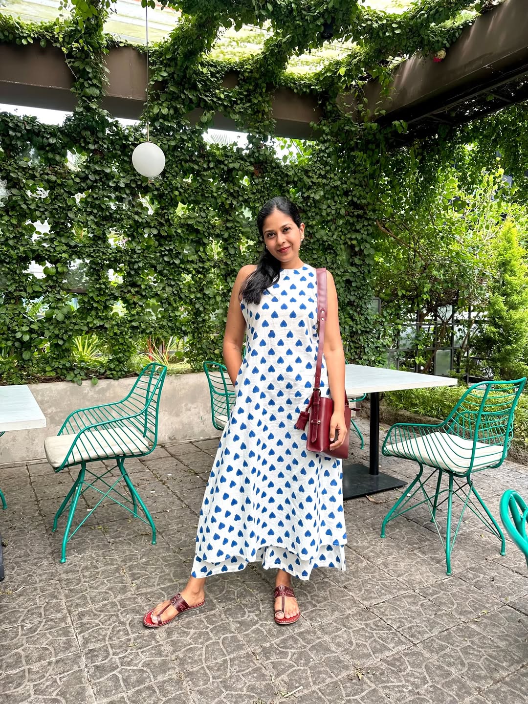Woman wearing a white and blue heart-printed ethnic maxi dress with a red handbag.