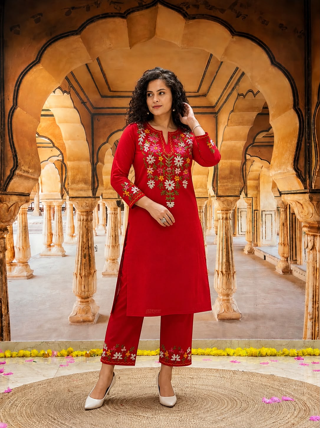 Woman wearing a red embroidered kurta and pant set in a traditional Indian palace setting.