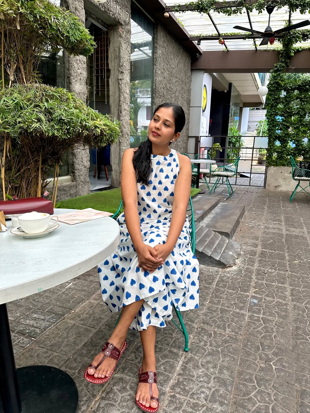 Woman wearing a white and blue heart-print sleeveless midi dress sitting at an outdoor cafe.