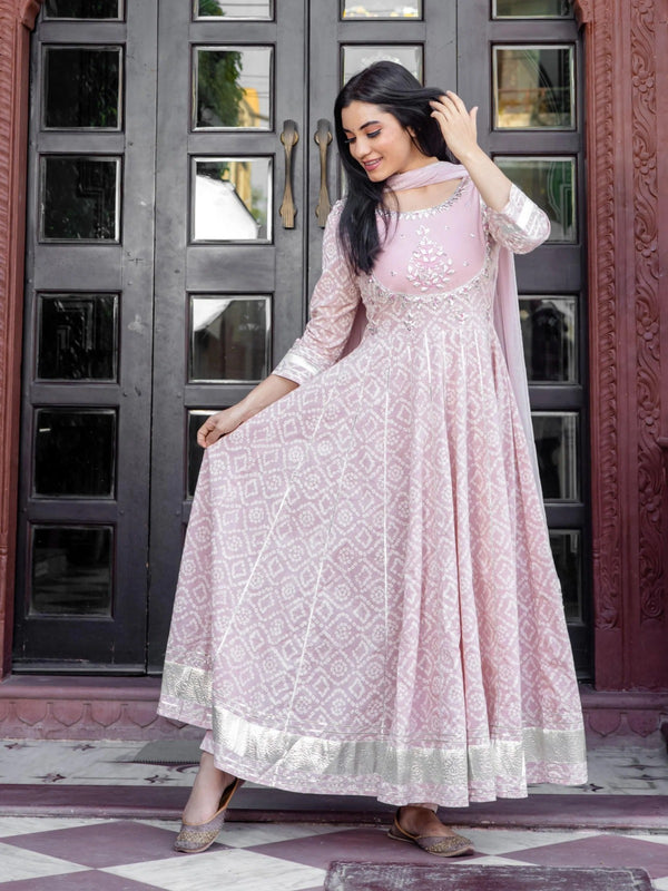 Woman wearing a light pink ethnic Anarkali suit with white bandhani print and silver border.