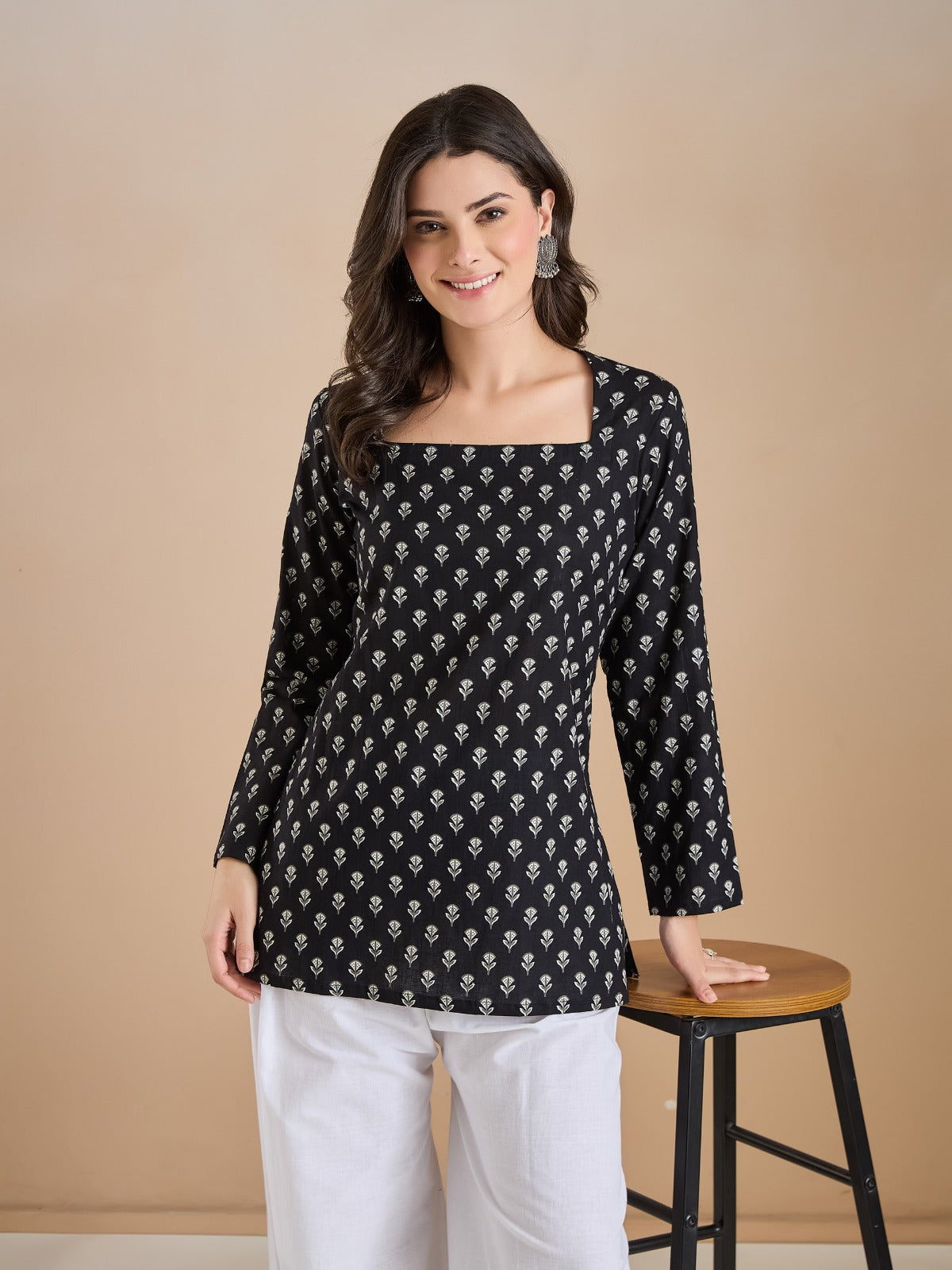 Woman wearing a black floral print tunic with white trousers