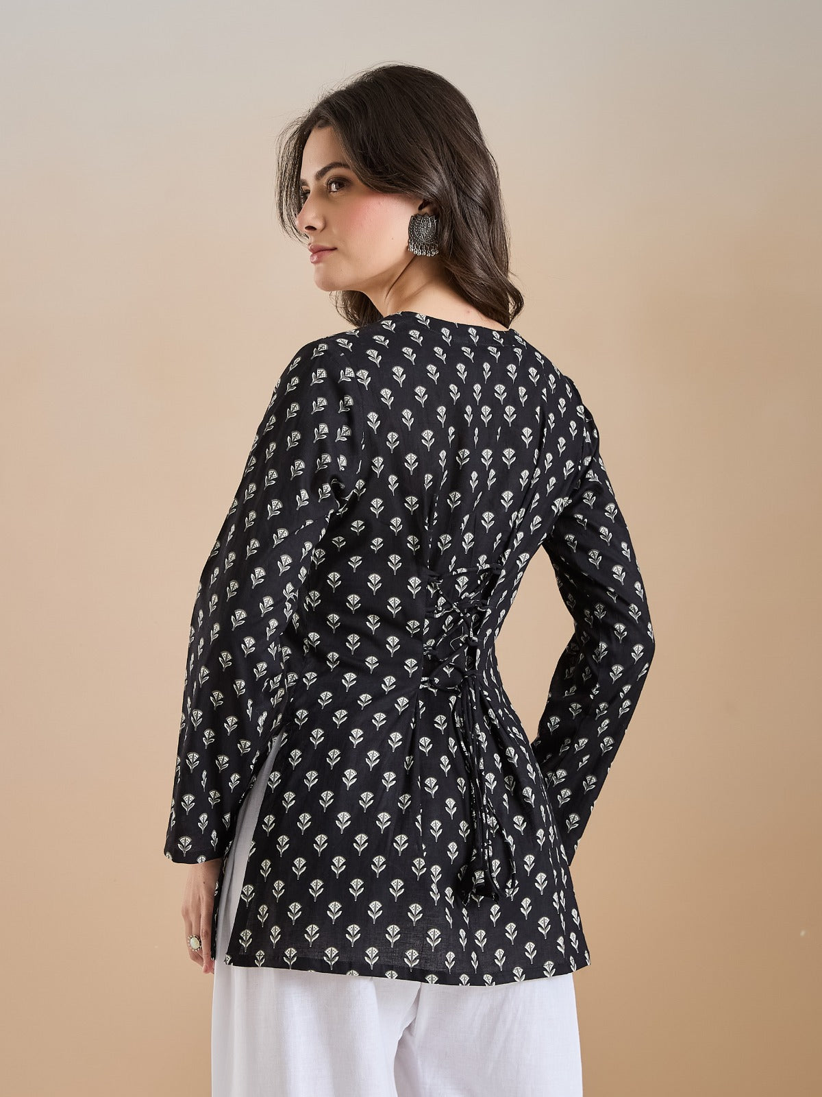 Woman wearing a black long-sleeve floral print tunic with tie-back detail and white trousers.