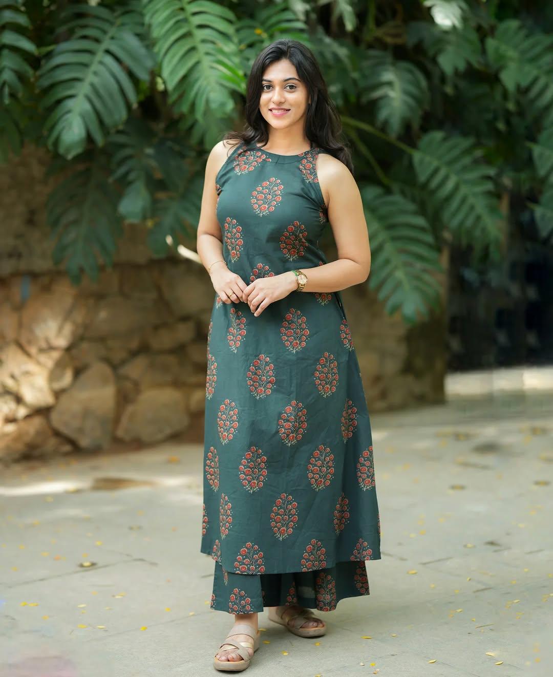 Woman wearing a dark green sleeveless Indian ethnic dress with red floral prints.