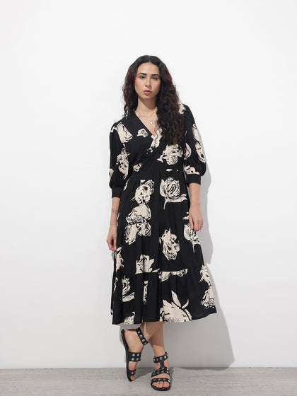 Woman wearing a black midi dress with large cream floral prints and long sleeves.