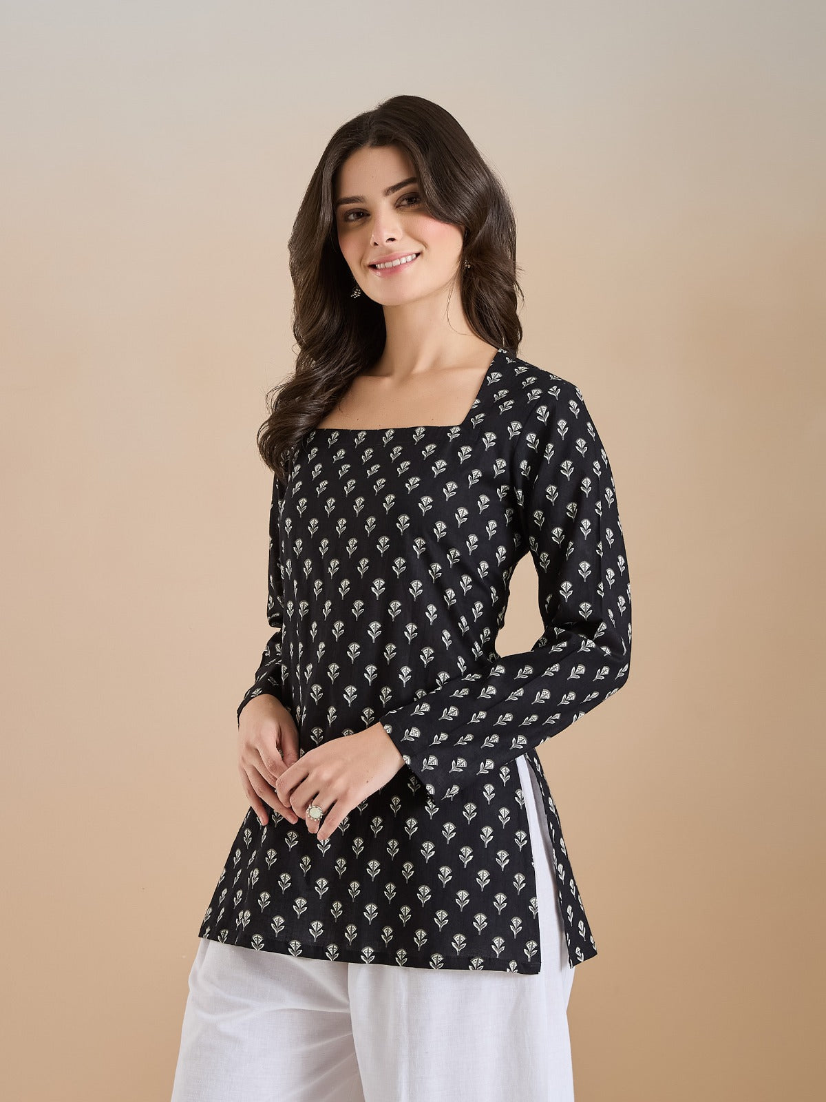 Woman wearing a black floral print long sleeve tunic with white trousers.