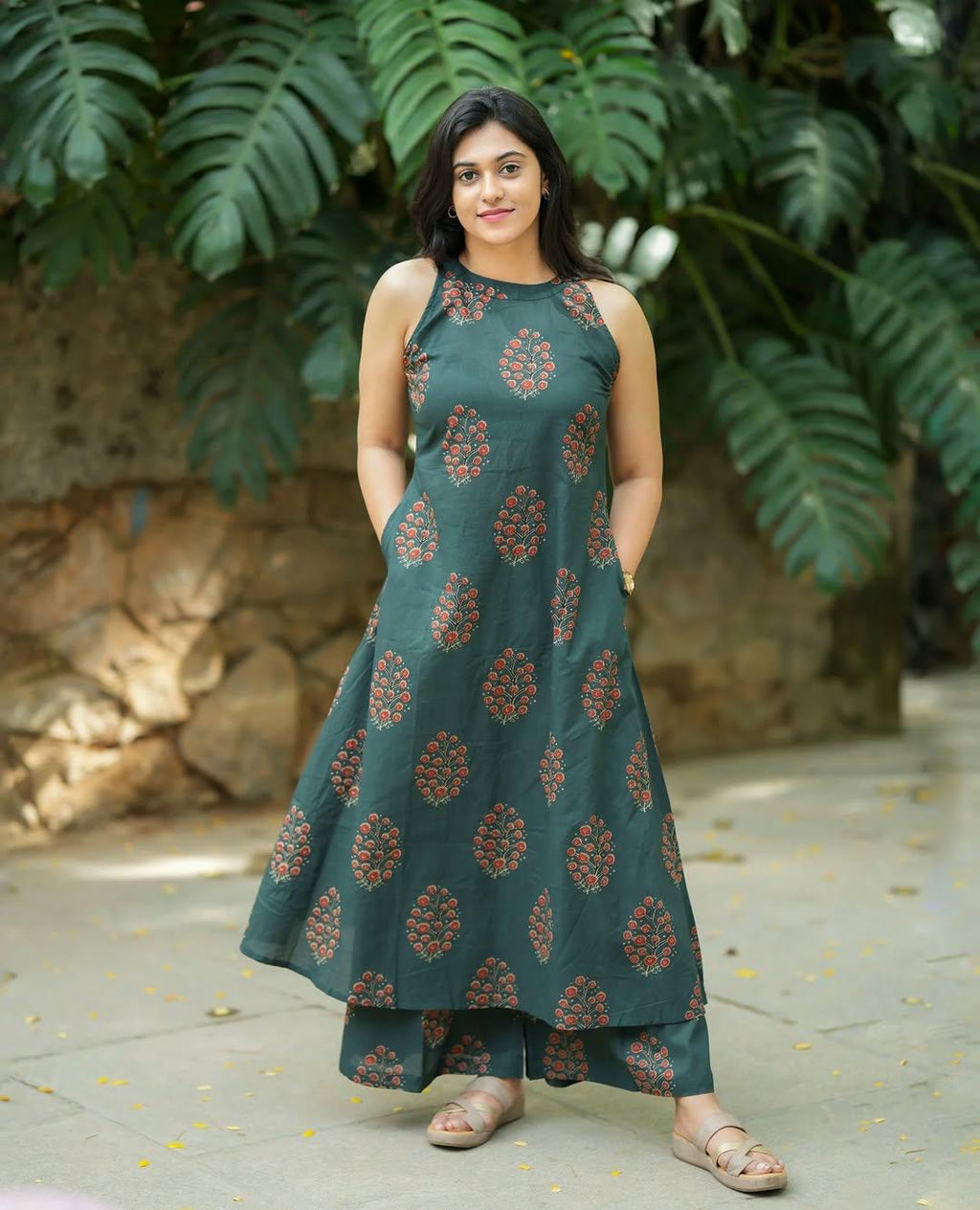 Woman wearing a dark green floral print ethnic halter neck dress and matching trousers.