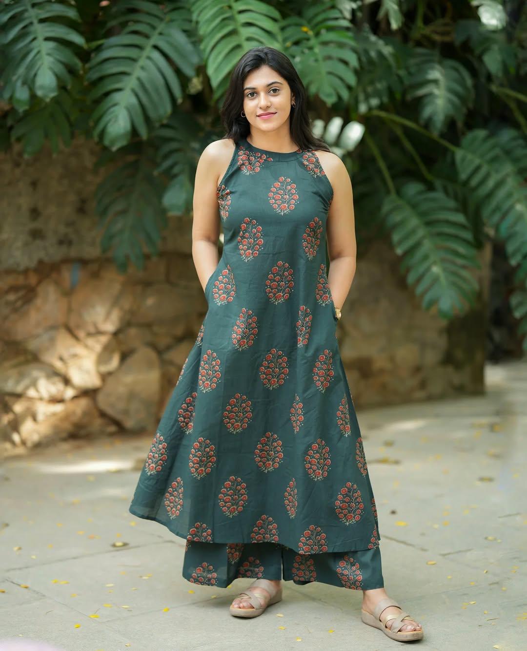 Woman wearing a dark green floral print ethnic halter neck dress and matching trousers.