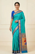 Woman wearing an elegant turquoise blue silk saree with gold zari border and traditional motifs.